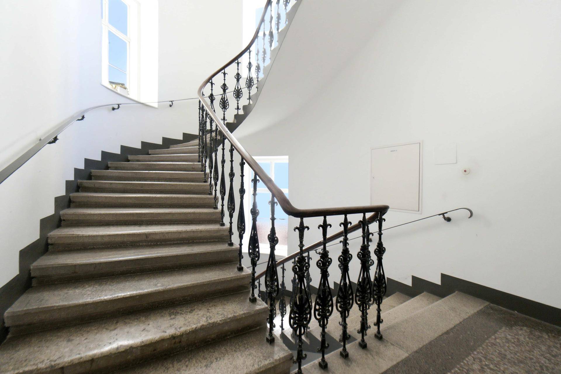 Weitläufiges Treppenhaus mit geschwungenem Geländer und großen Fenstern für viel Licht.