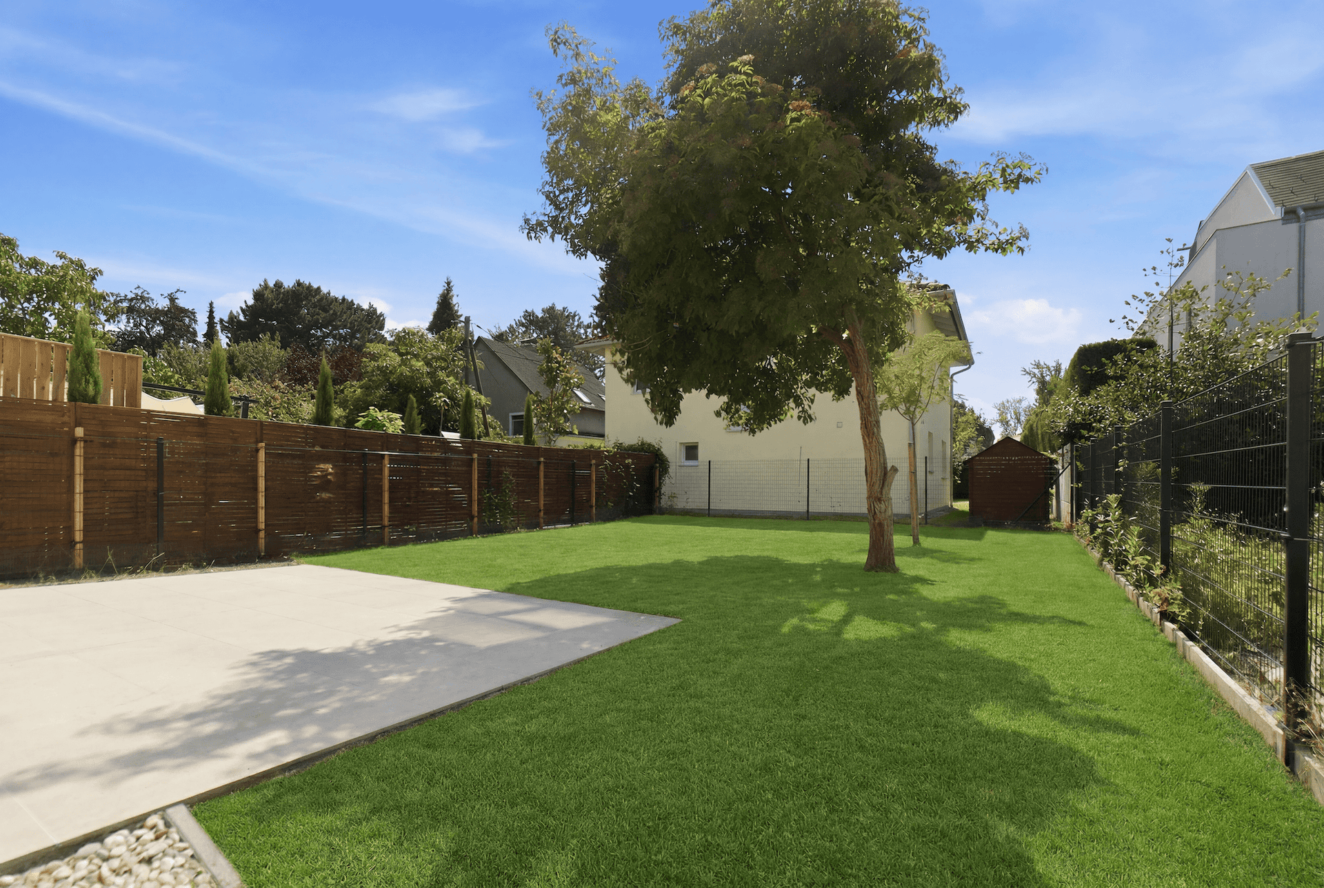 Gepflegter Gartenbereich mit Rasen, Baum und gepflasterter Terrasse hinter dem Haus.