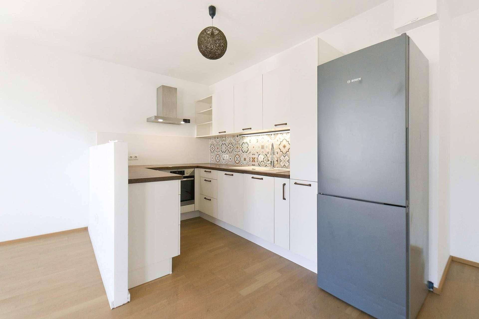 Moderne Einbauküche mit weißen Schränken, gemustertem Fliesenspiegel und Kühlschrank.