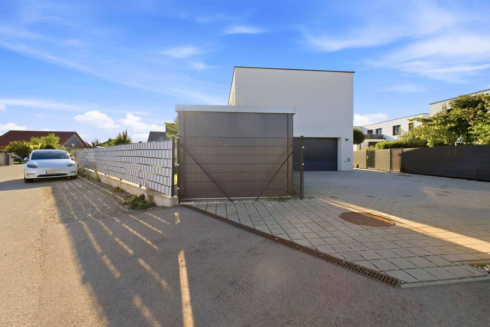 Zufahrt zum modernen Haus mit gepflastertem Bereich und Zaun.