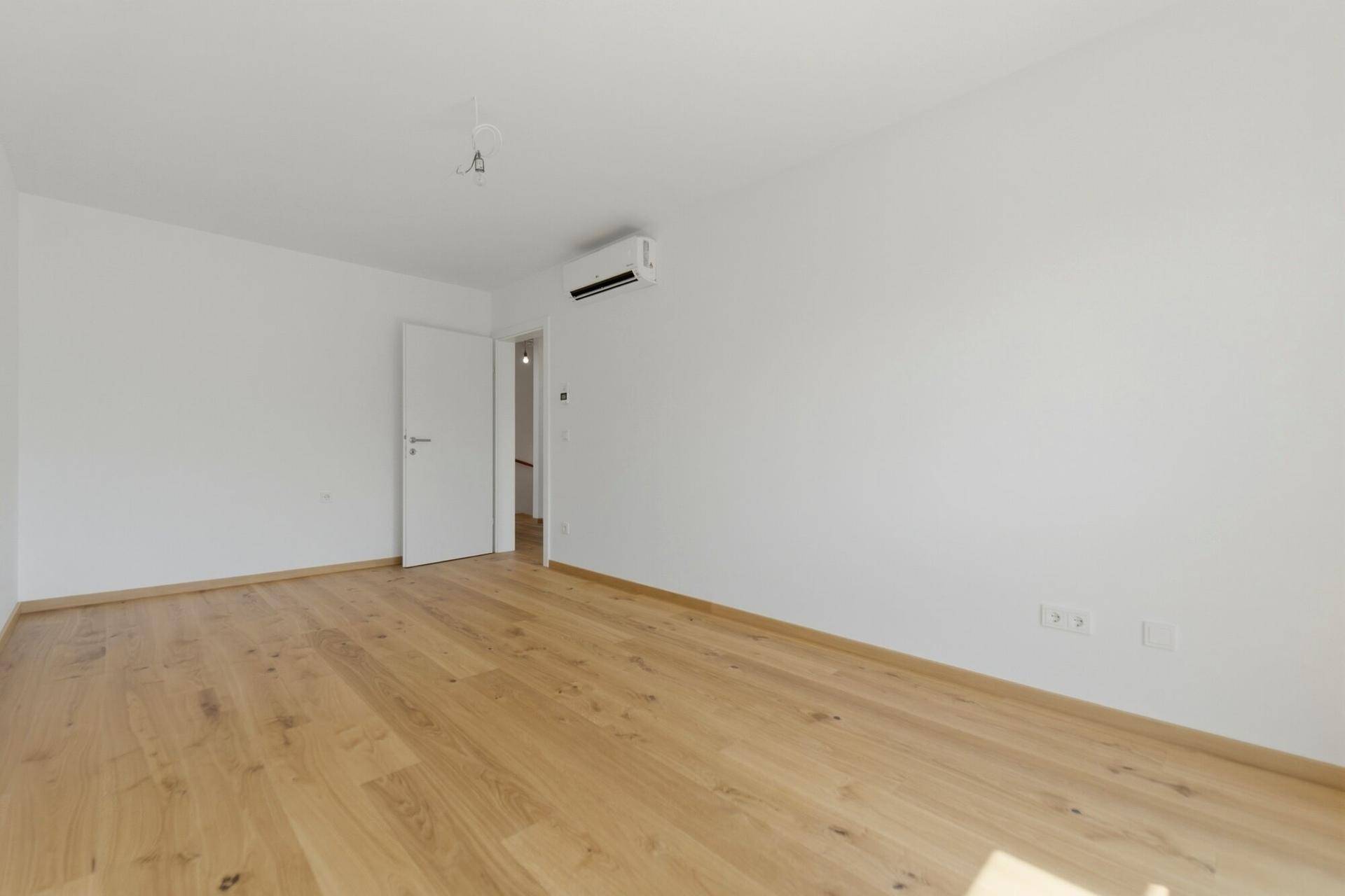 Leeres Zimmer mit Holzboden und weiß gestrichenen Wänden, bereit zur individuellen Gestaltung.