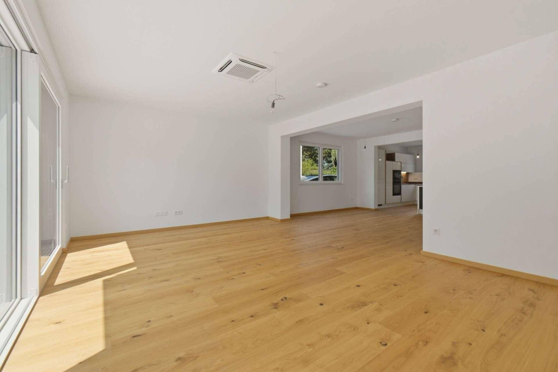 Geräumiger offener Wohn-Essbereich mit Holzboden und Deckenklimaanlage, ideal für geselliges Beisammensein.