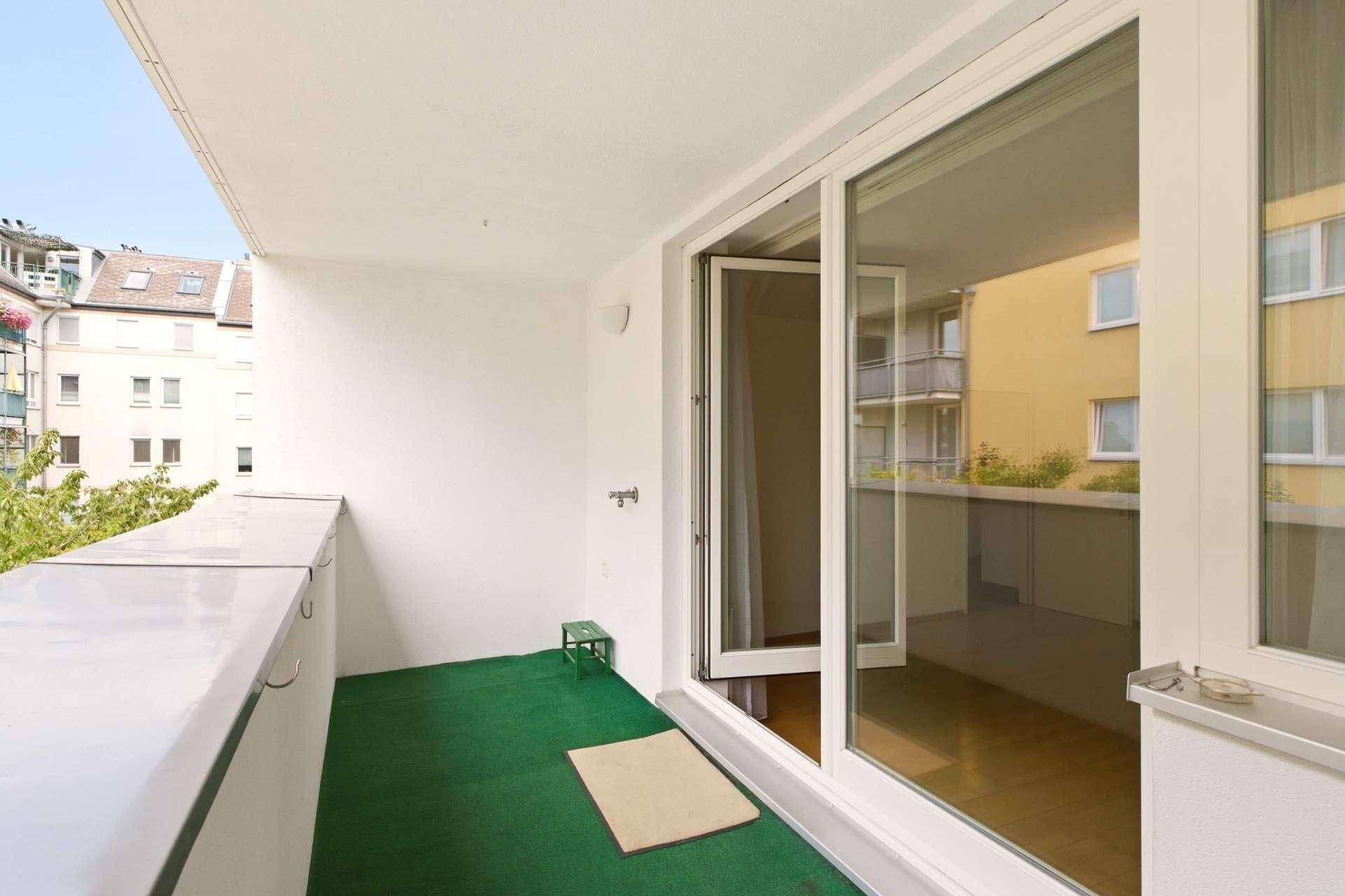 Balkon mit Kunstrasen und Ausblick auf die Nachbargebäude, ideal für Entspannung im Freien.
