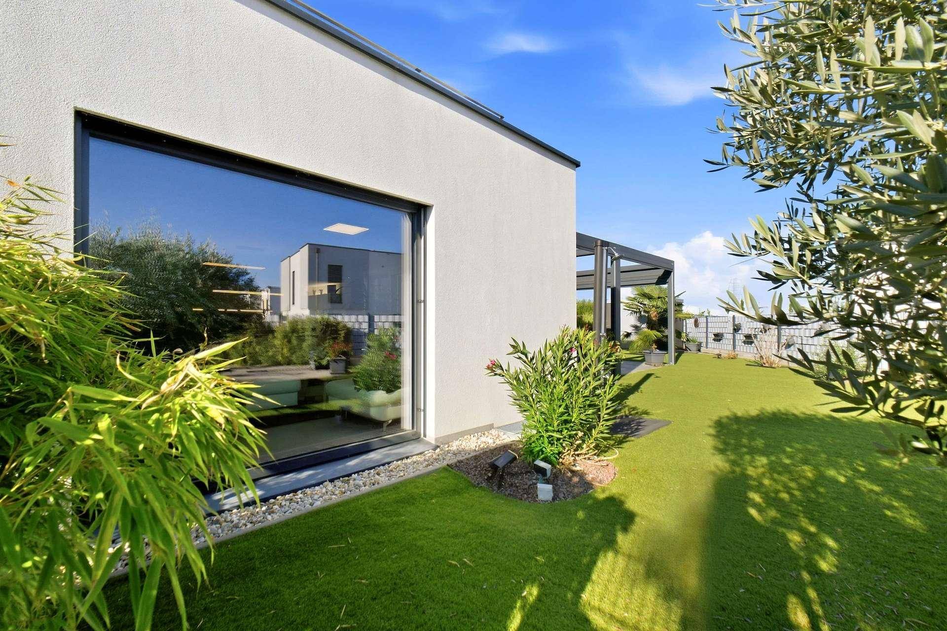 Moderne Hausfassade mit großen Fenstern und gepflegtem Gartenbereich.