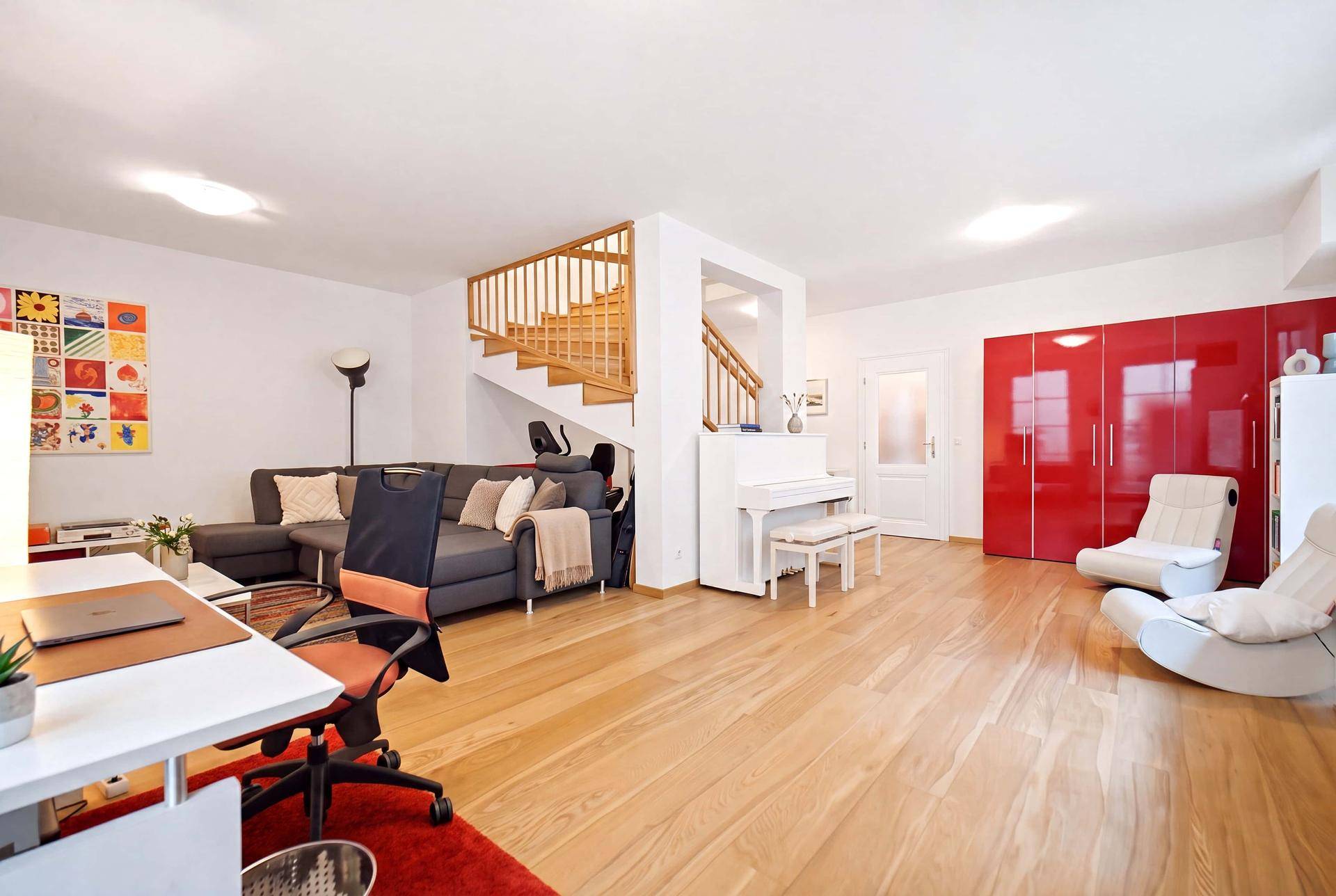 Geräumiger Wohnbereich mit Holzboden, Treppe, rotem Schrank und Klavier, offen gestaltet.