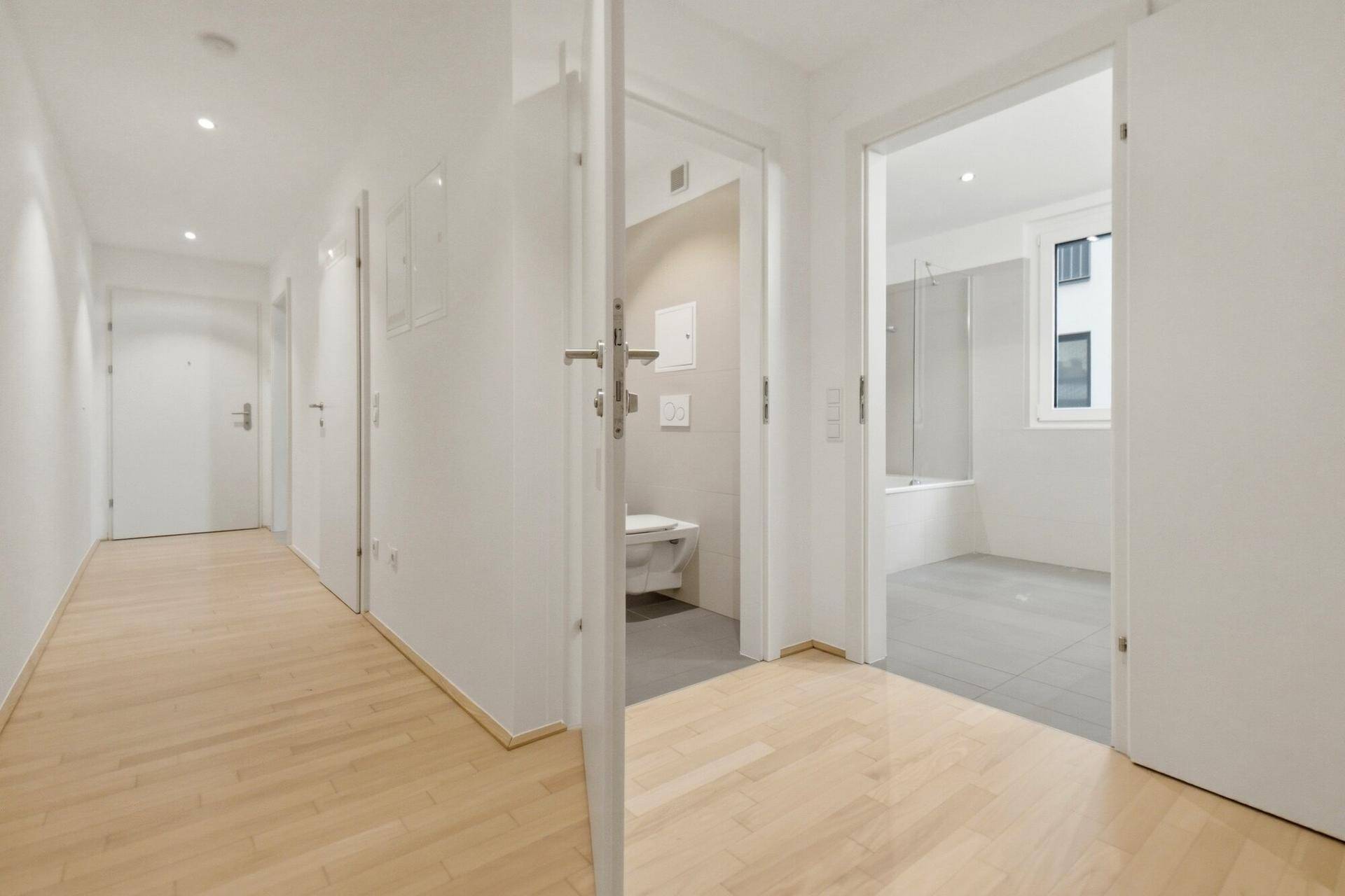 Heller Flur mit Holzboden, der zu einem Gäste-WC und einem Badezimmer führt.
