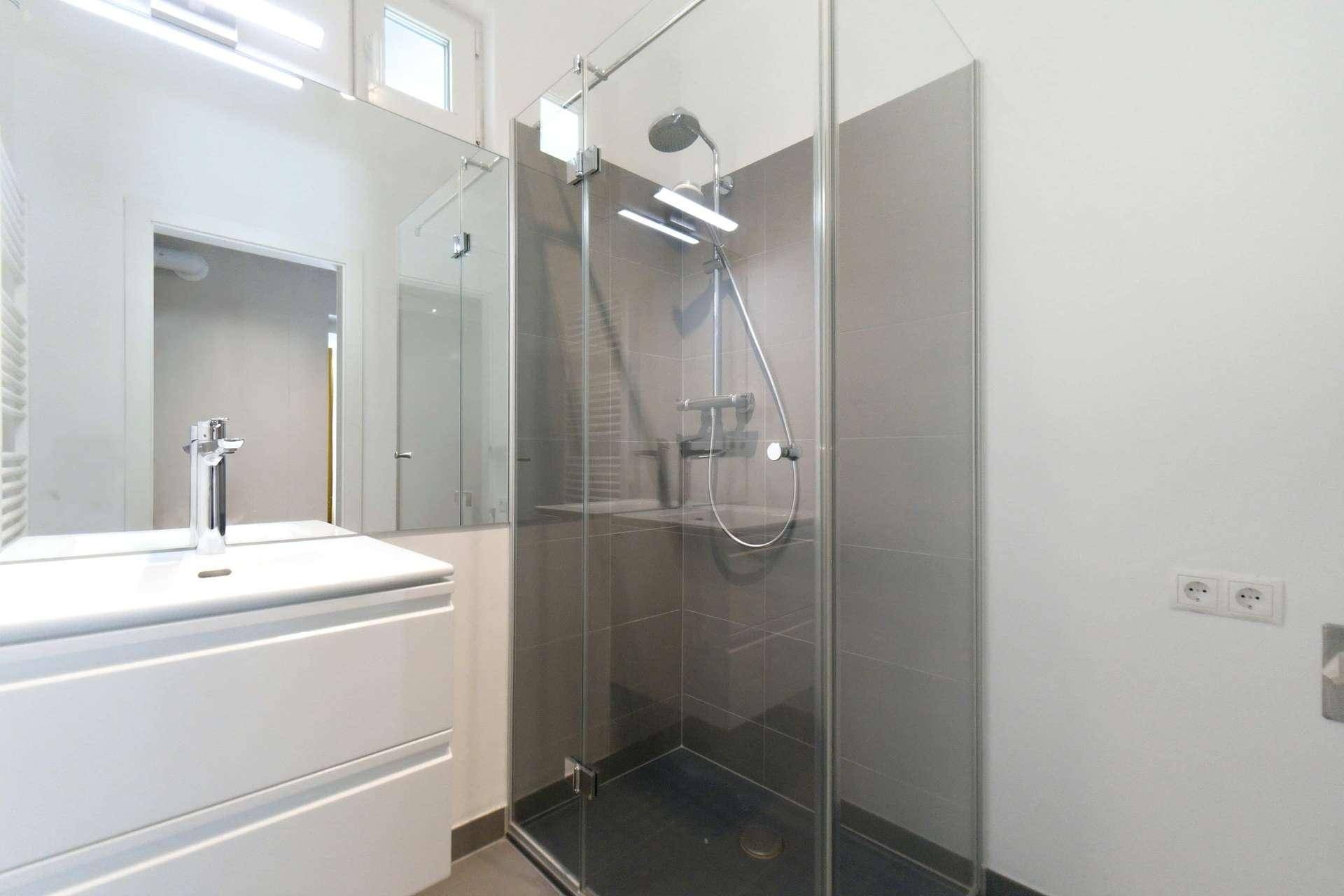 Modernes Badezimmer mit begehbarer Dusche, großem Spiegel und Fenster.
