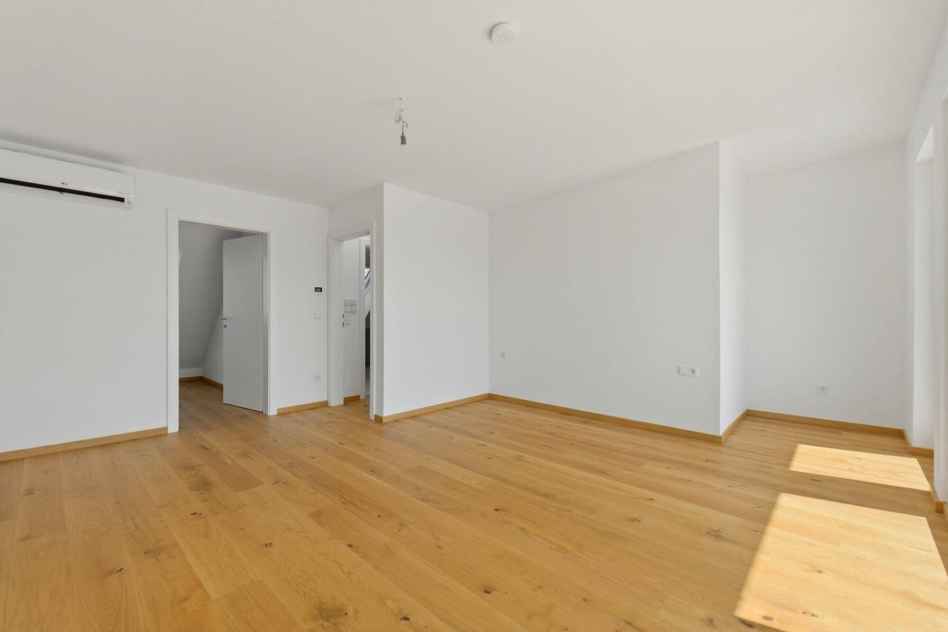 Leeres Schlafzimmer mit Eichenparkett, Klimaanlage und offenem Zugang zum Treppenhaus.