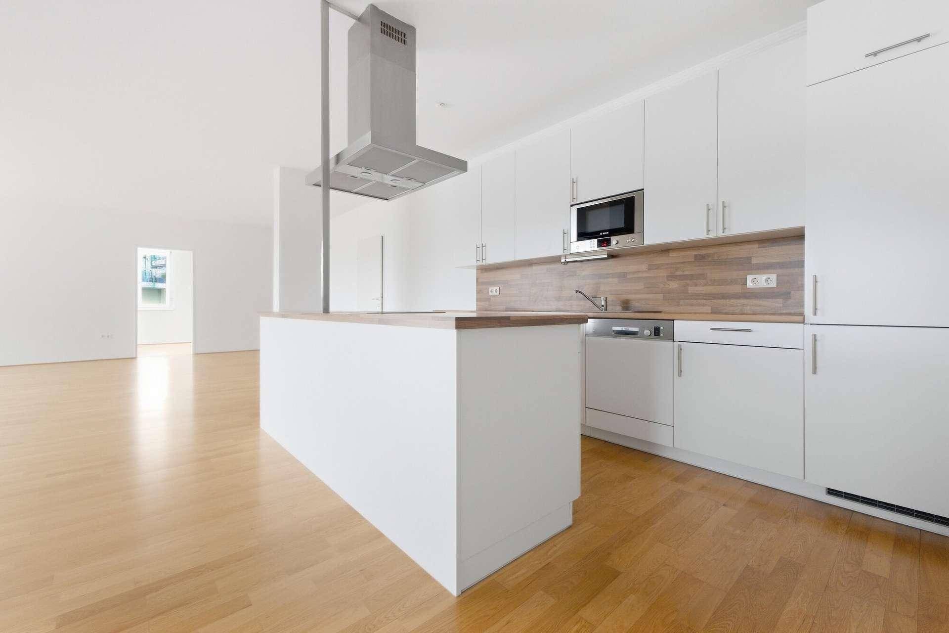 Moderne Einbauküche mit weißen Fronten, Holz-Arbeitsplatten und integrierten Geräten wie Mikrowelle und Geschirrspüler.