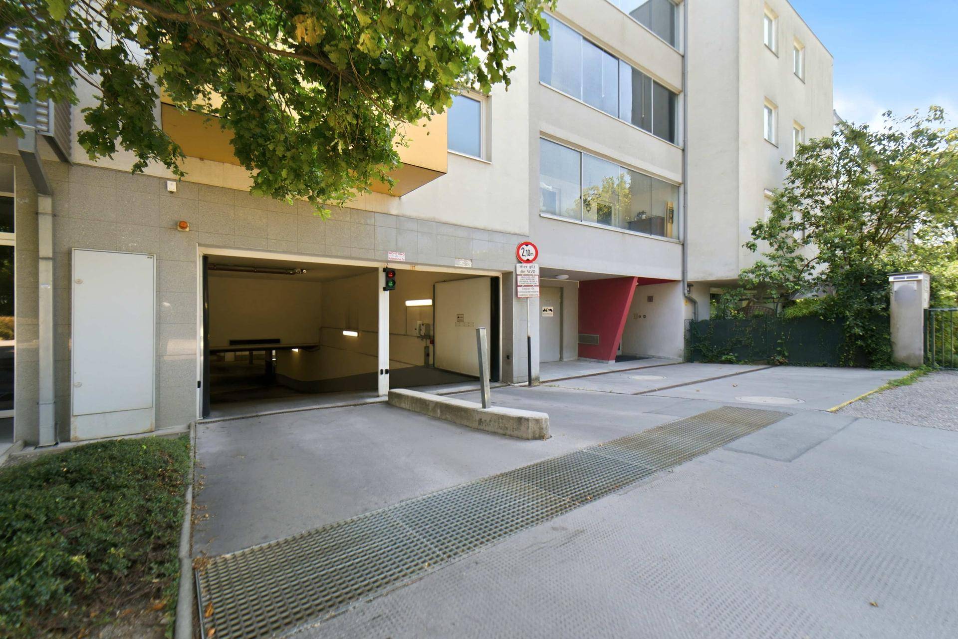Eingangsbereich zur Tiefgarage eines modernen Wohngebäudes mit Schranke und Zufahrt.