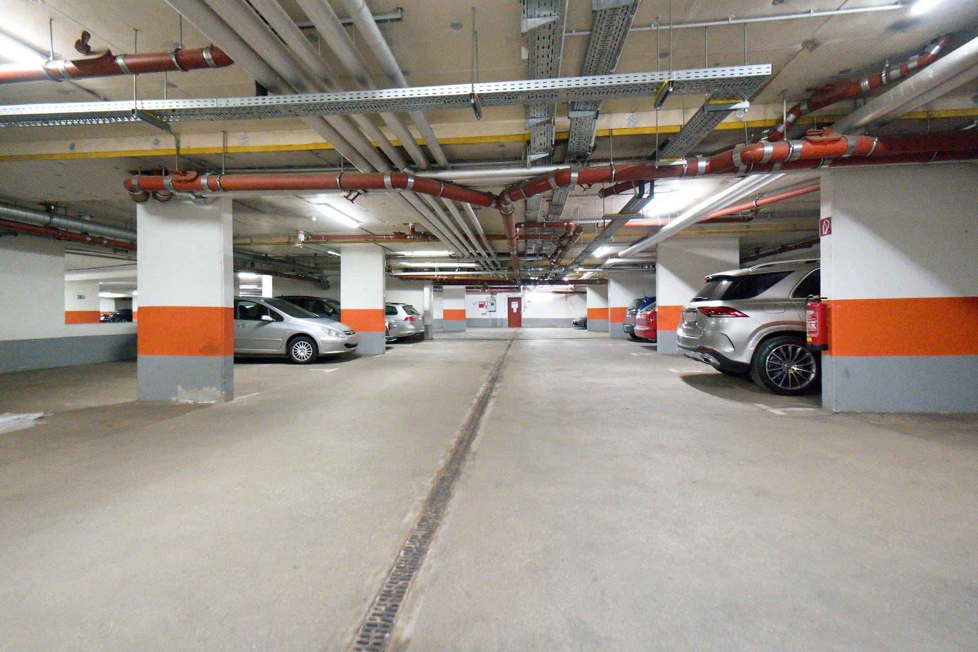 Geräumige Tiefgarage mit mehreren Stellplätzen, Betonboden und sichtbaren Installationen an der Decke.