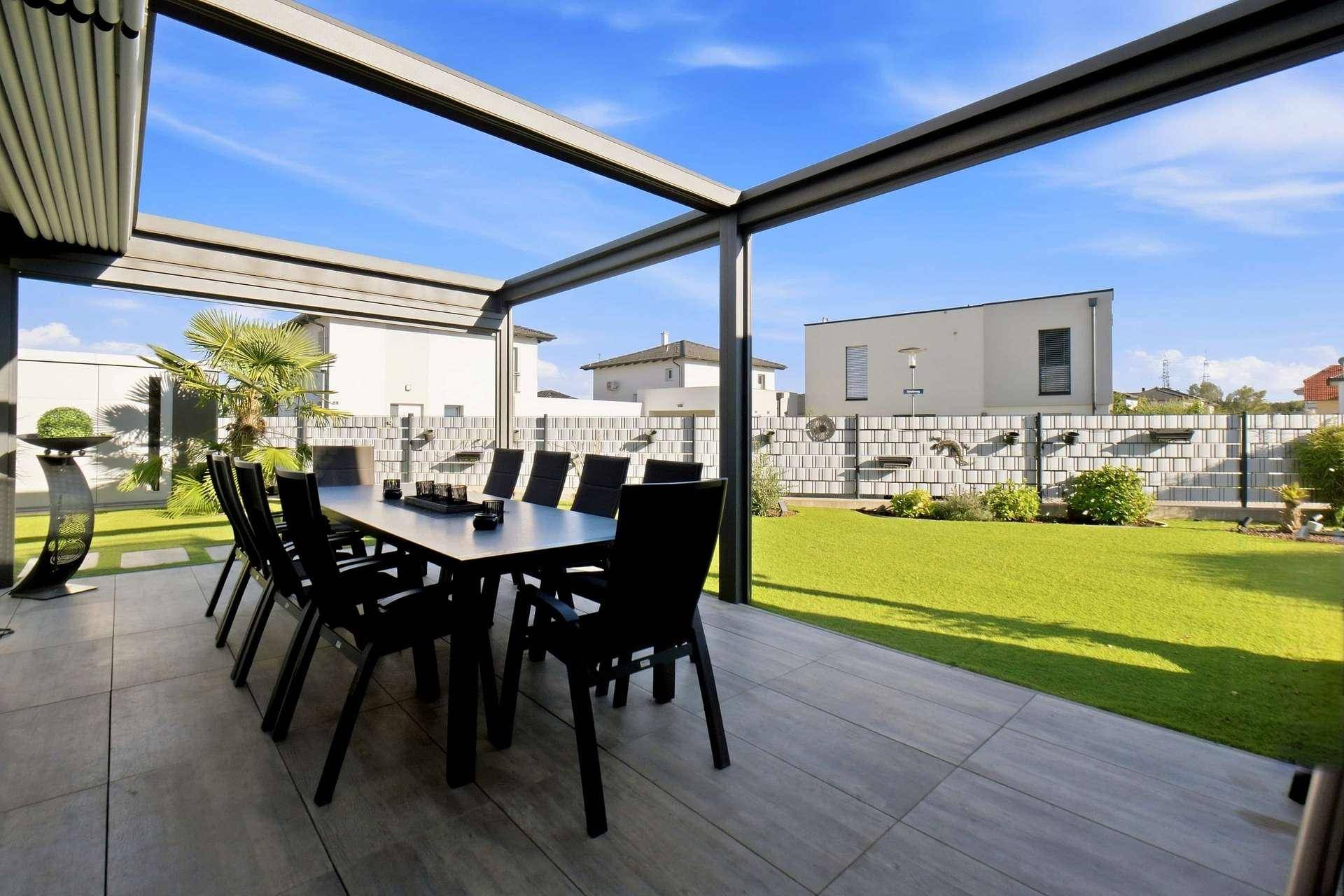 Sonnige Terrasse mit Esstisch unter einer Pergola und Blick auf den Garten.