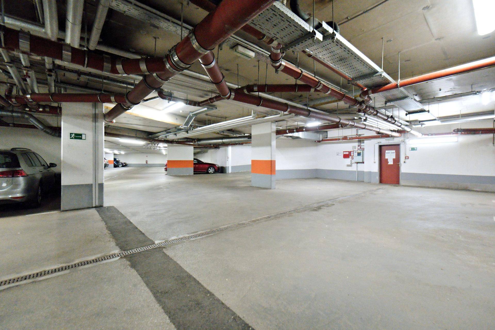 Geräumige Tiefgarage mit mehreren Stellplätzen, Betonboden und sichtbaren Installationen an der Decke.