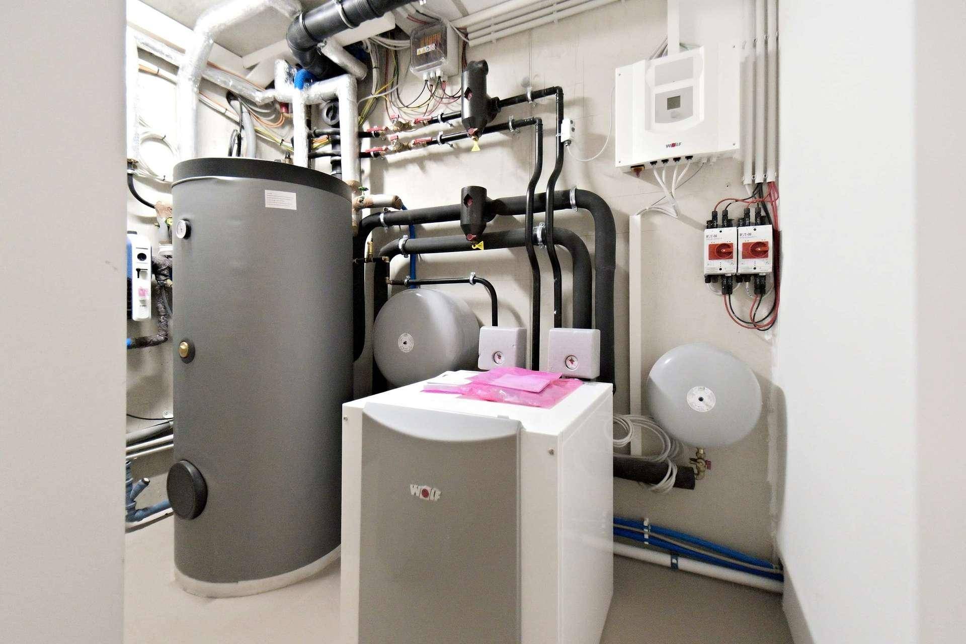 Funktionaler Technikraum mit Heizungsanlage, Warmwasserspeicher und zahlreichen Leitungen.