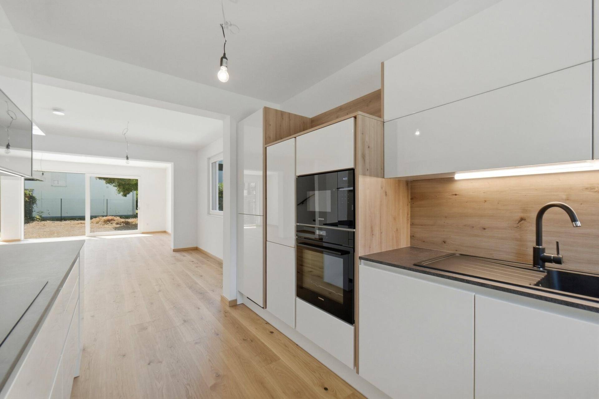 Helle Einbauküche mit weißen Schränken, Holzelementen und Blick in den offenen Wohnbereich.