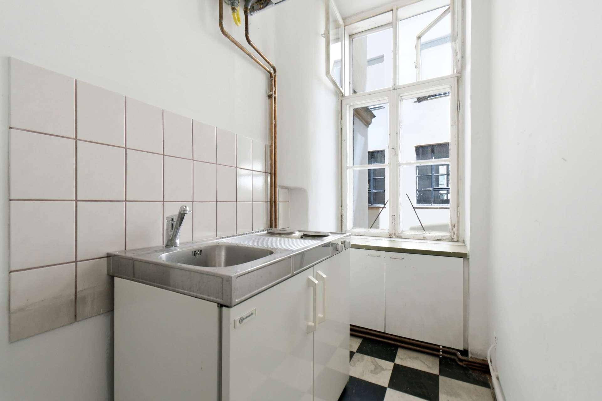 Kleine Küche mit Spüle, Kochfeld, weißen Unterschränken und Fenster zum Innenhof.