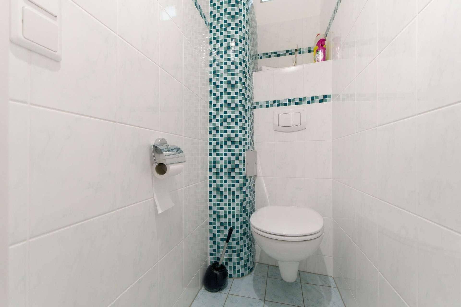 Kleines WC mit Wand-WC und weißen Fliesen, akzentuiert durch grüne Mosaikfliesen.
