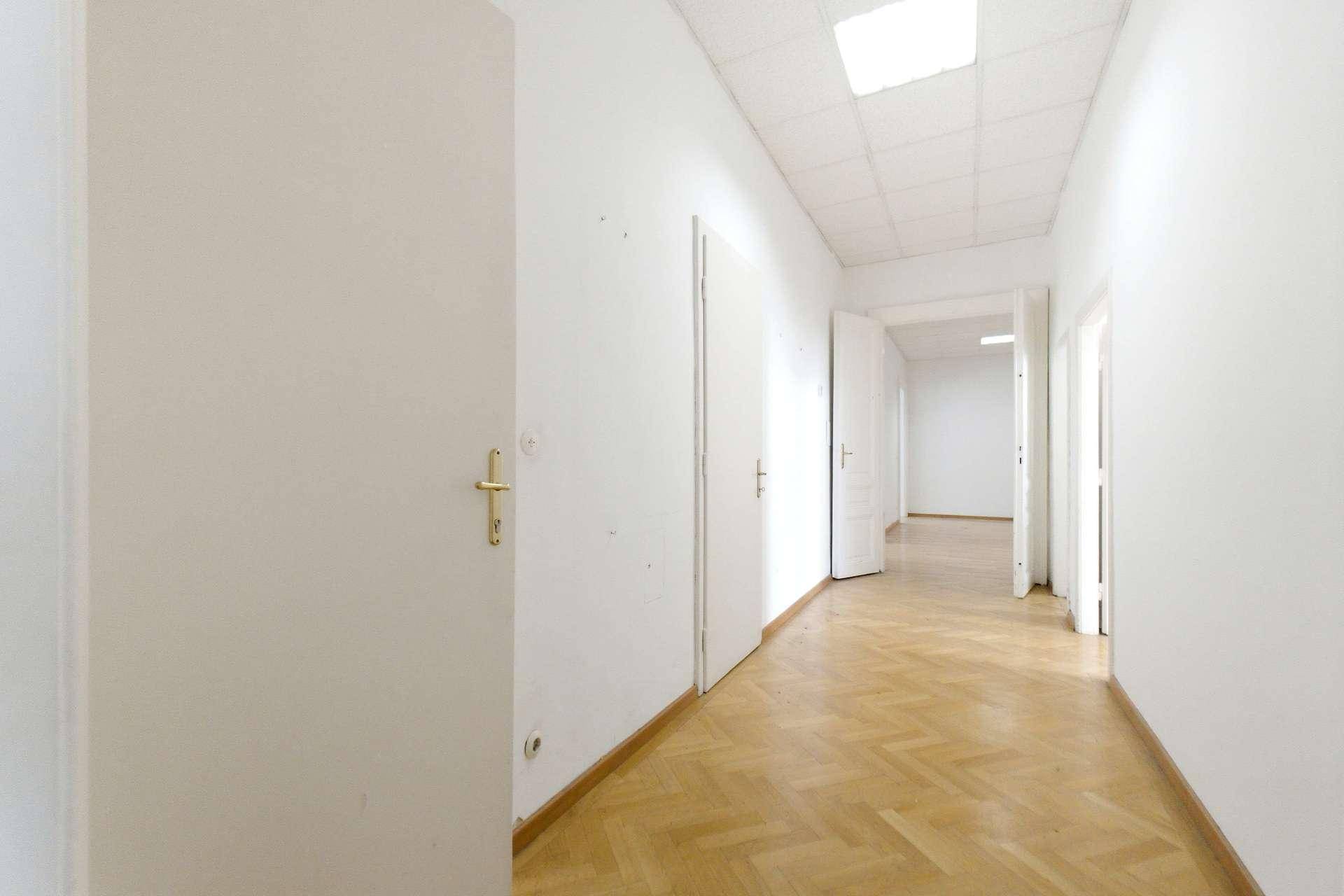 Langer, heller Flur mit Fischgrätparkett und mehreren weißen Türen, klassisches Ambiente.