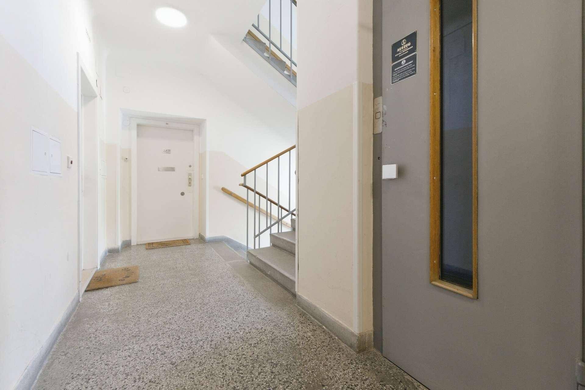 Heller Treppenhausbereich mit Terrazzoboden, Treppe und Aufzug im Mehrfamilienhaus.