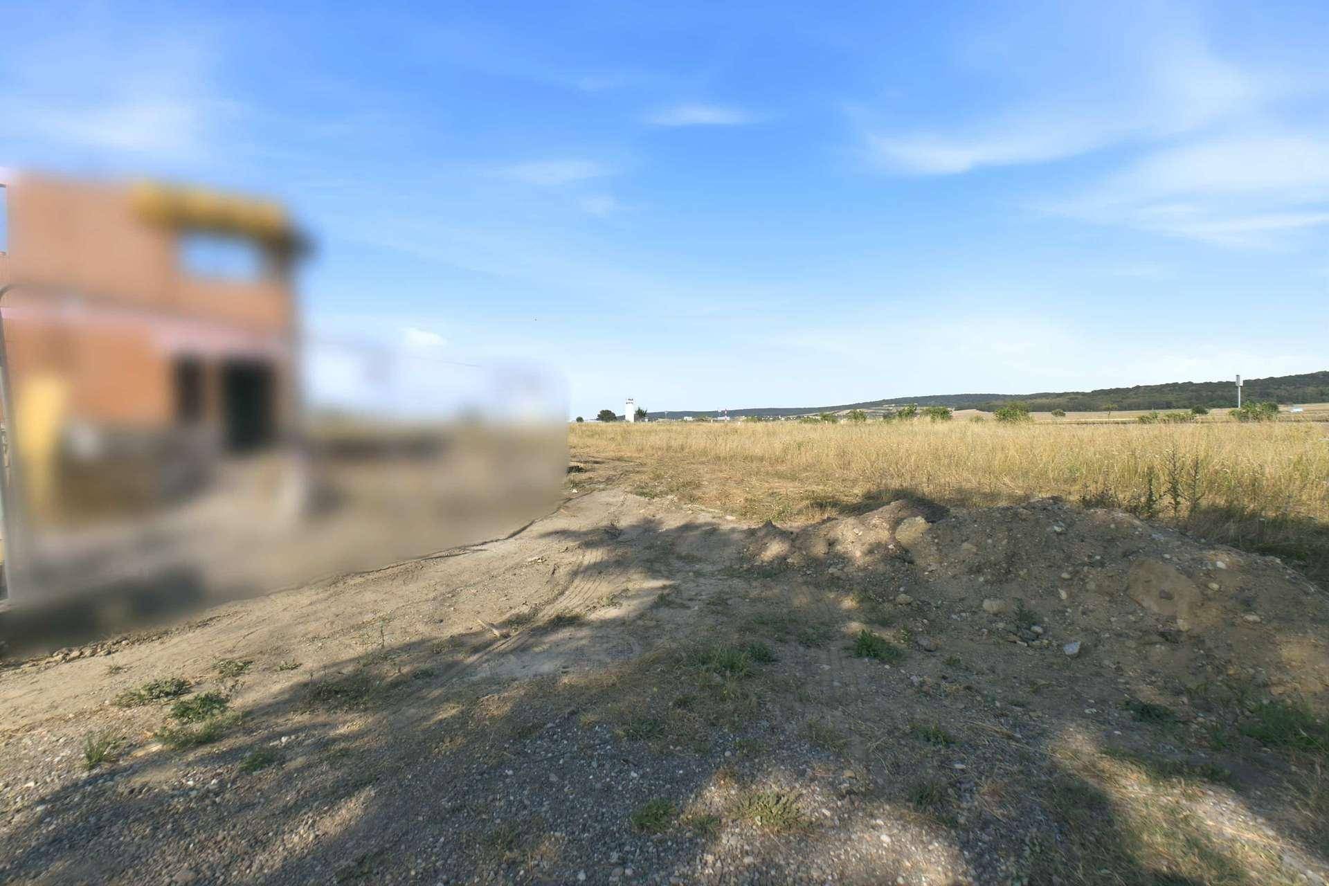 Weitläufiges Feld mit trockenem Gras und einem unscharfen Gebäude im Hintergrund.
