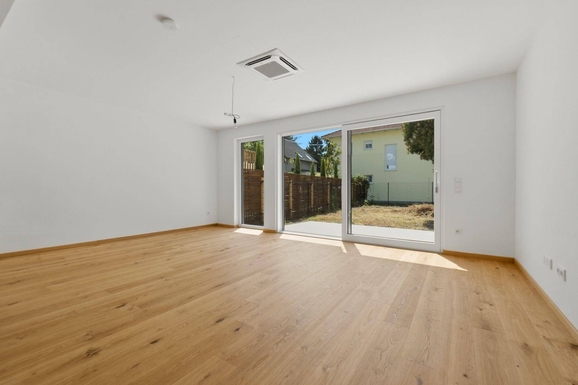 Geräumiges, leeres Wohnzimmer mit Eichenparkett, Klimaanlage und Gartenzugang.