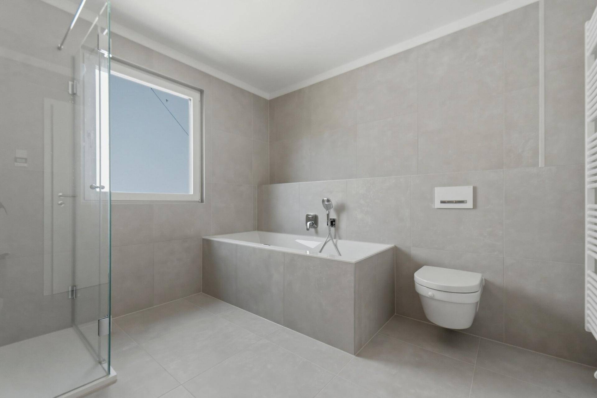 Modernes Badezimmer mit Badewanne, Hänge-WC, Dusche und Fenster für Tageslicht.