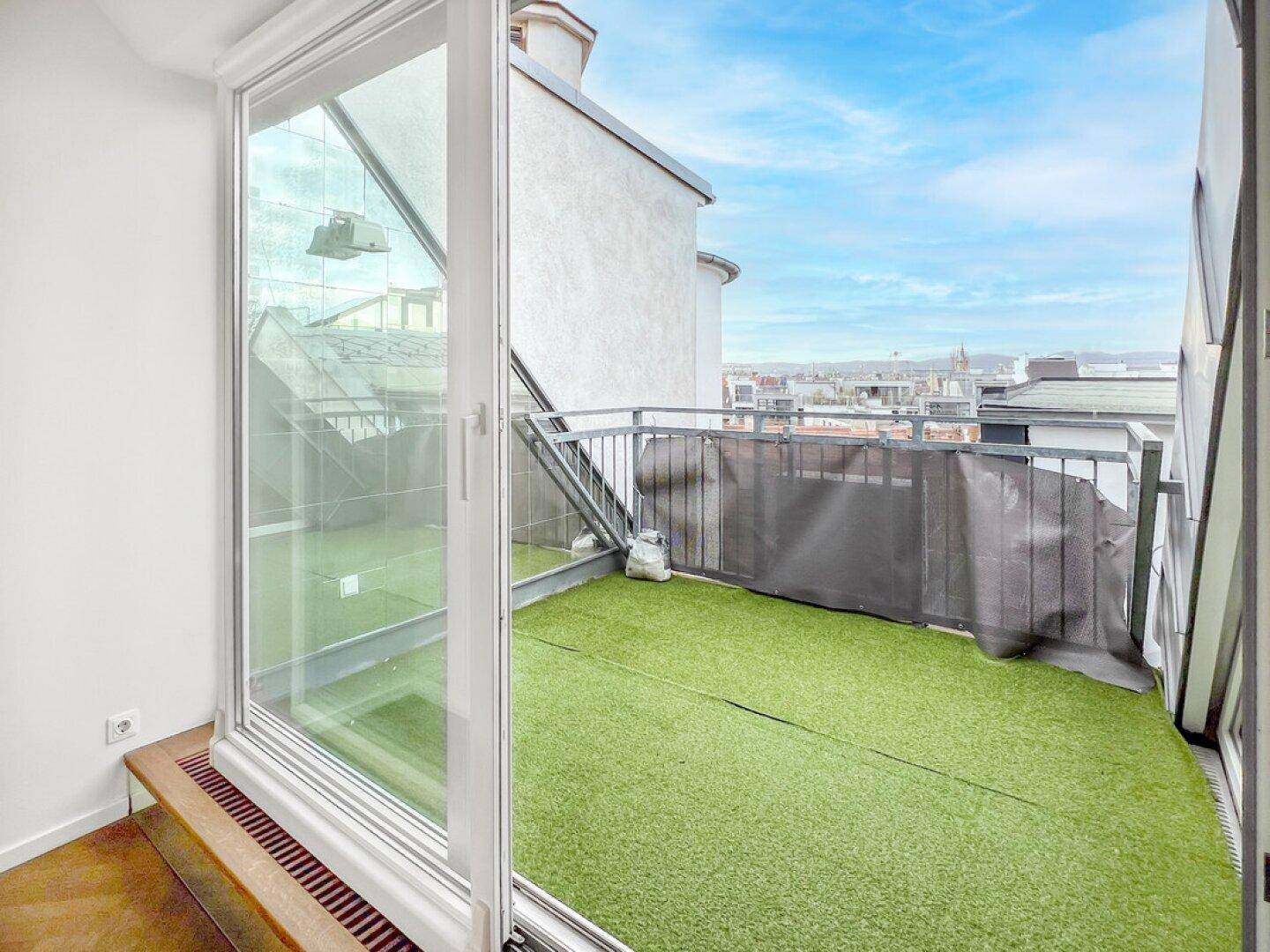 Dachbalkon mit Kunstrasen und Panoramablick auf die Stadt und den Himmel.
