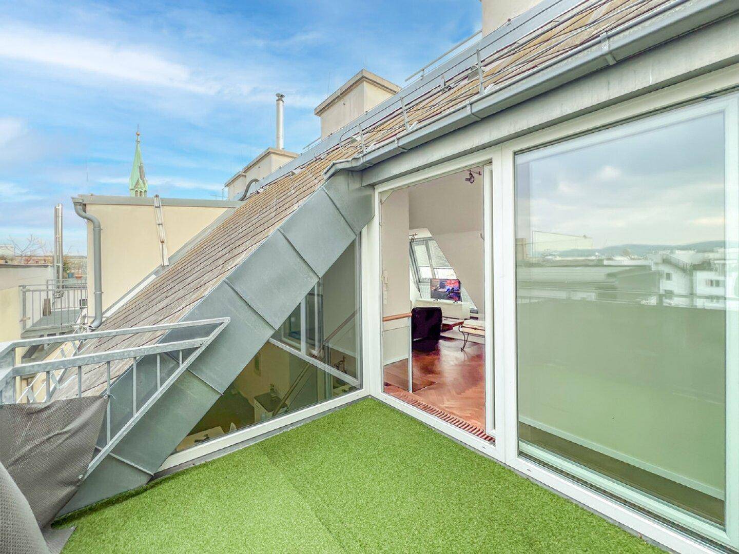 Kleiner Balkon mit Kunstrasen und weitem Blick über die Dächer der Stadt.