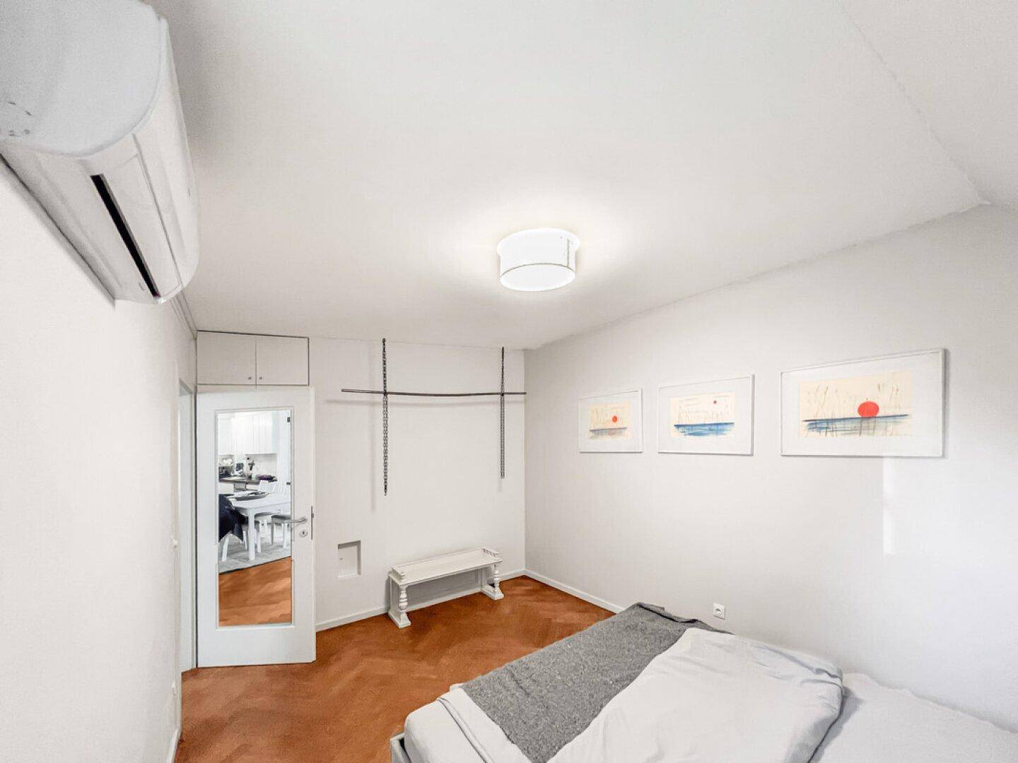 Schlafzimmer mit Klimaanlage, Parkettboden und Zugang zu einem weiteren Raum.