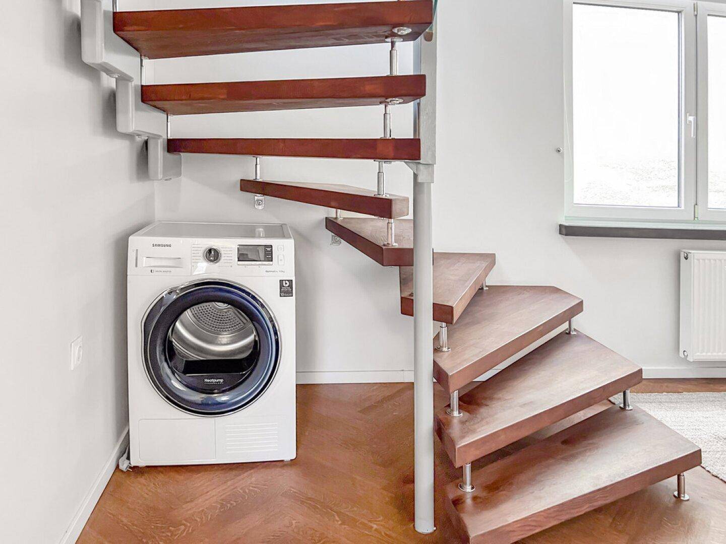 Bereich mit Waschmaschine und Trockner unter einer modernen Holztreppe.