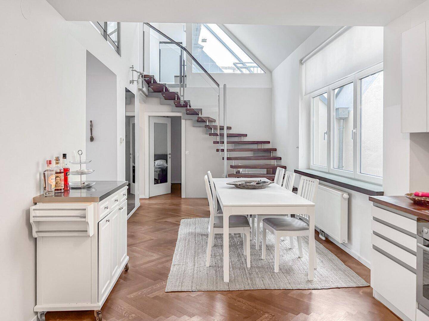 Offener Essbereich mit Holzboden, Esstisch und moderner Treppe zu einer oberen Etage.