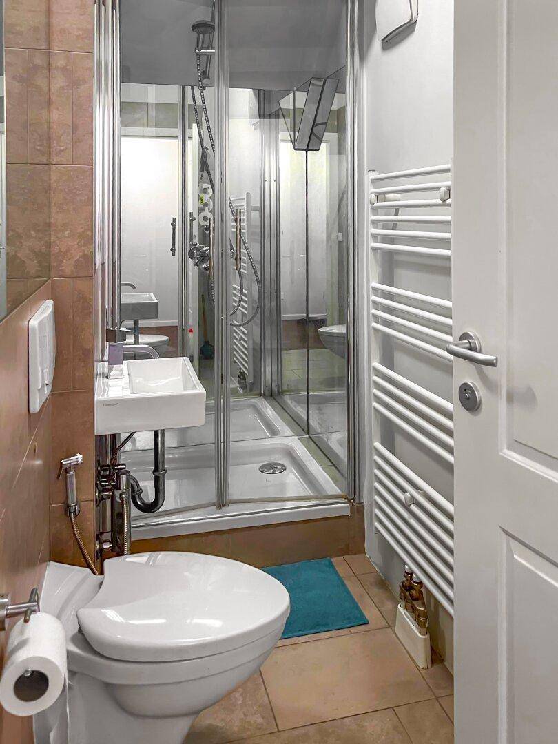 Kleines Badezimmer mit Dusche, WC, Waschbecken und beheiztem Handtuchhalter.