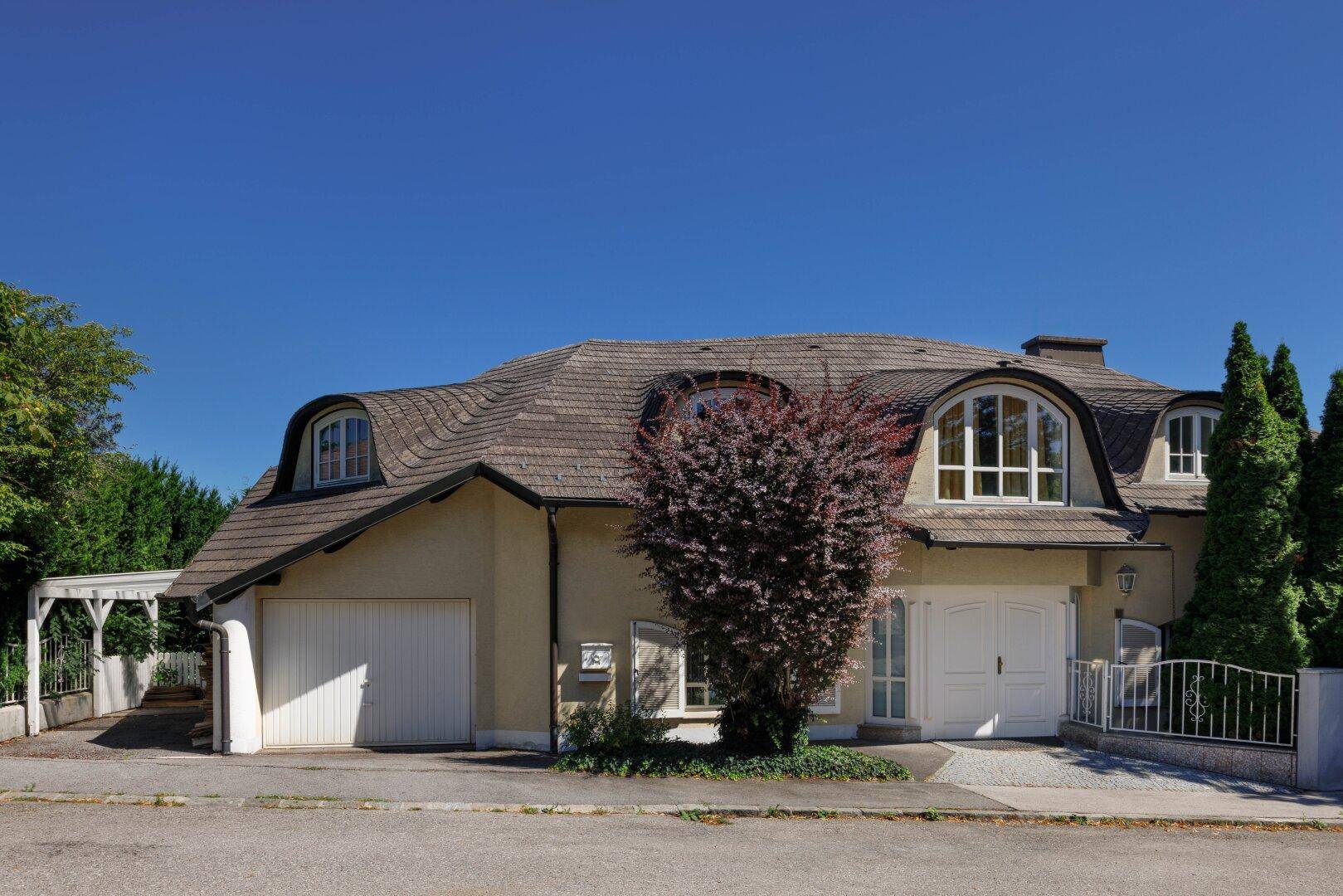 Elegantes Haus mit markantem Mansarddach, geschwungenen Gaubenfenstern und integrierter Garage.