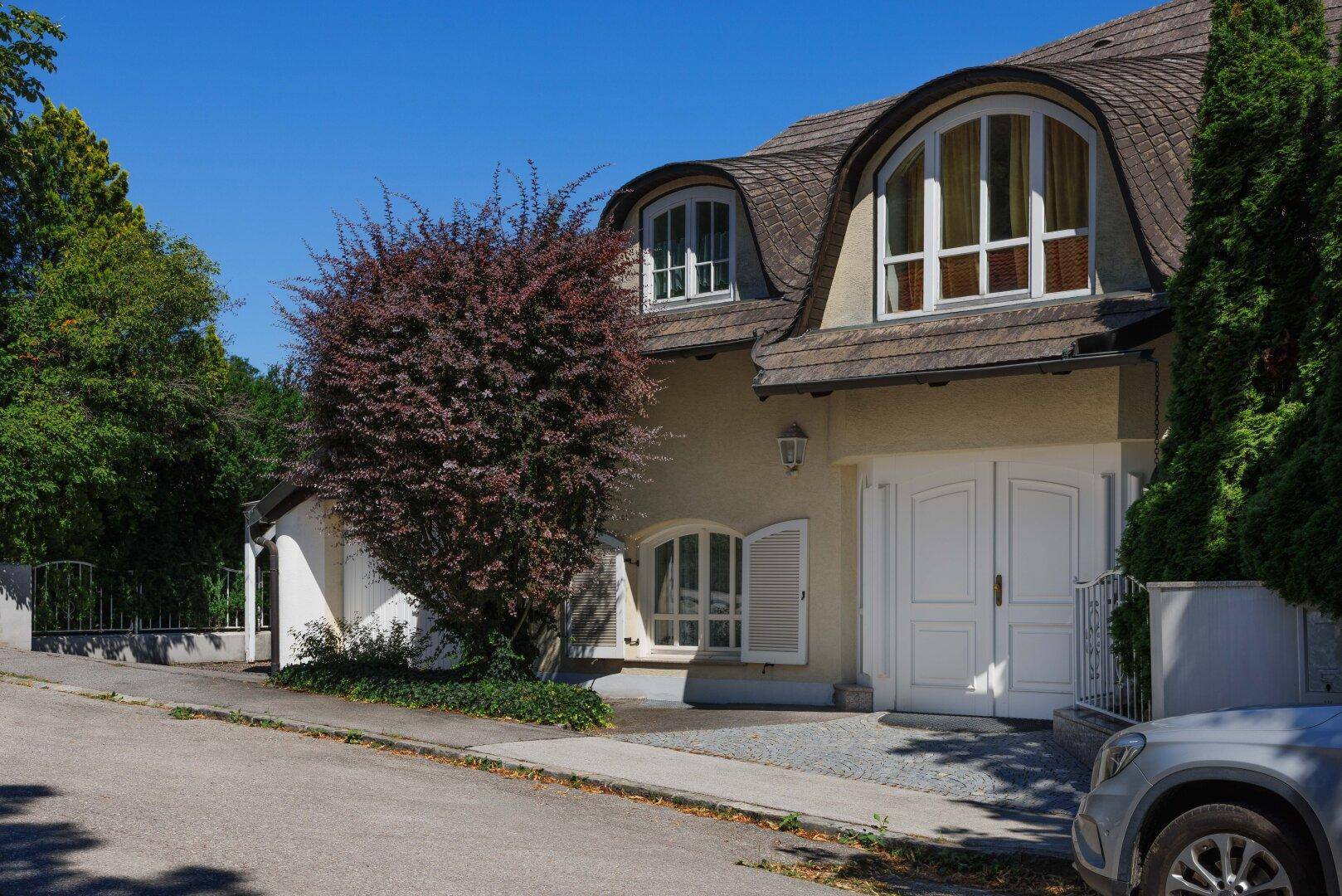 Elegante Hausfassade mit geschwungenem Dach, großen Fenstern und Doppelgaragentor.