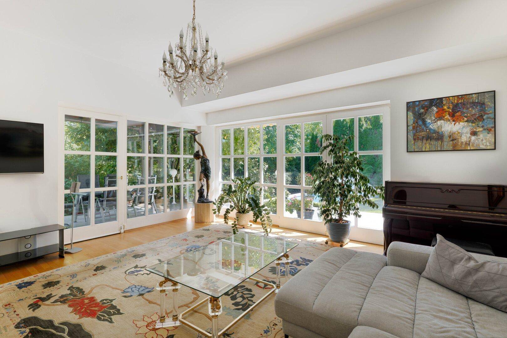 Lichtdurchflutetes Wohnzimmer mit großen Fenstern, Holzboden und Zugang zur Terrasse.