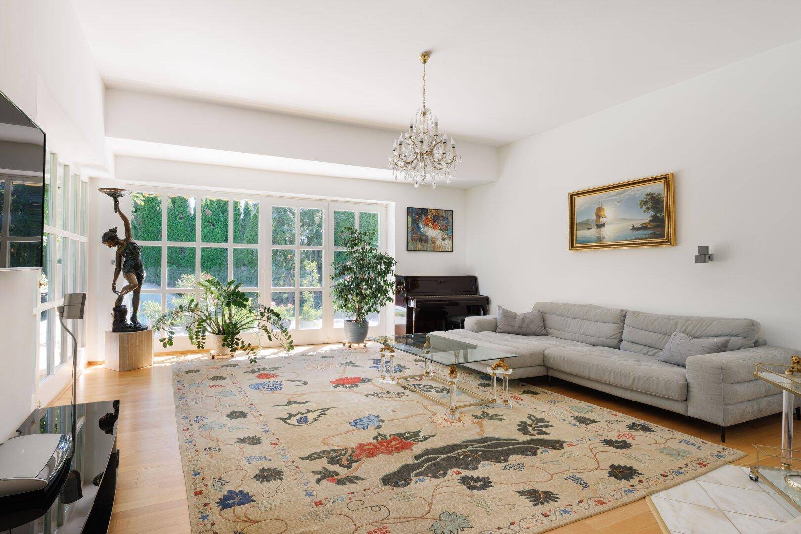 Helles Wohnzimmer mit großem Teppich, bequemer Couch und Blick in den grünen Garten.