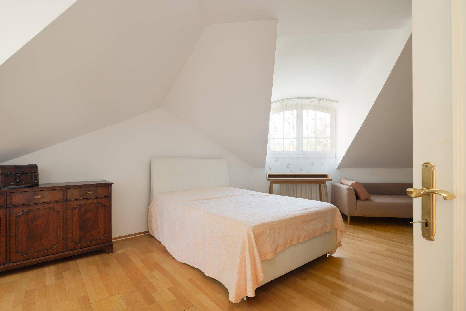 Ruhiges Schlafzimmer im Dachgeschoss mit Holzboden, Fenster und klassischem Mobiliar.