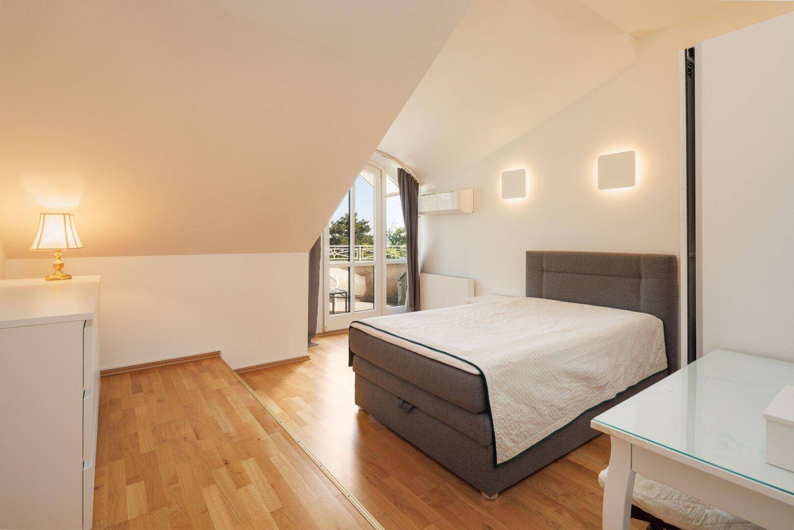 Modern eingerichtetes Schlafzimmer mit Holzboden, Klimaanlage und Balkonzugang.
