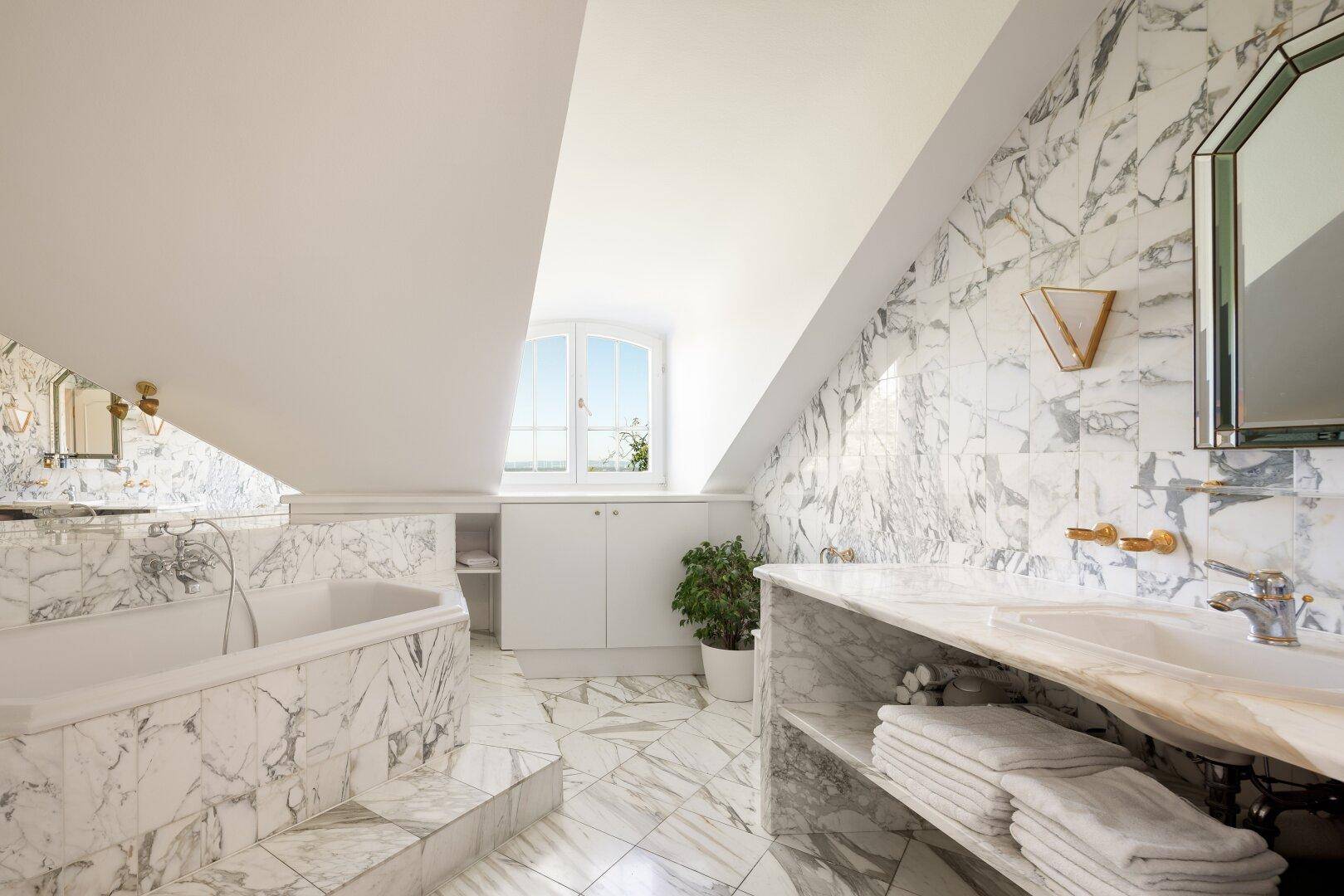 Luxuriöses Badezimmer im Dachgeschoss mit Marmorfliesen, Badewanne und Doppelwaschbecken.