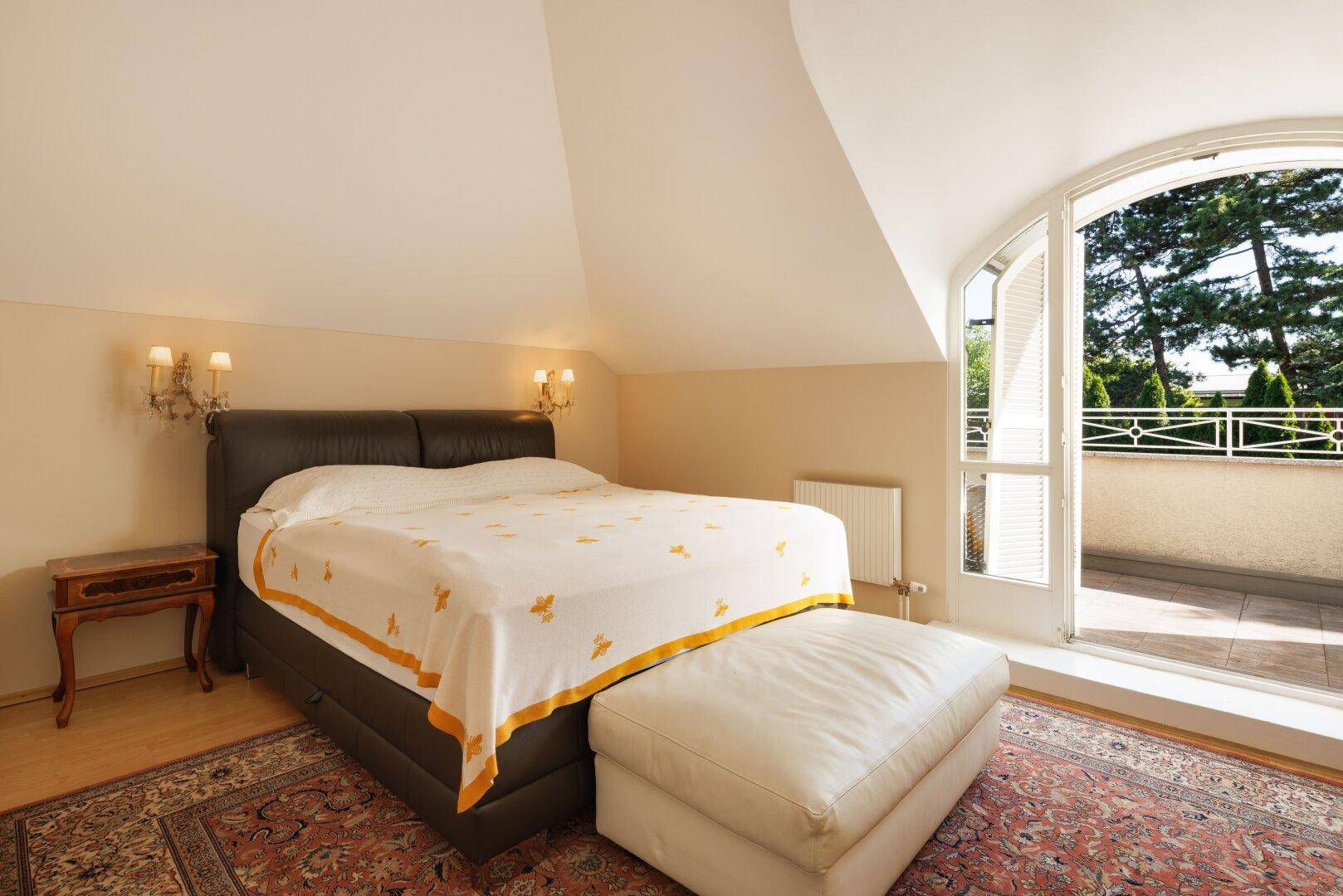Gemütliches Schlafzimmer im Dachgeschoss mit Zugang zu einem kleinen Balkon und Holzboden.