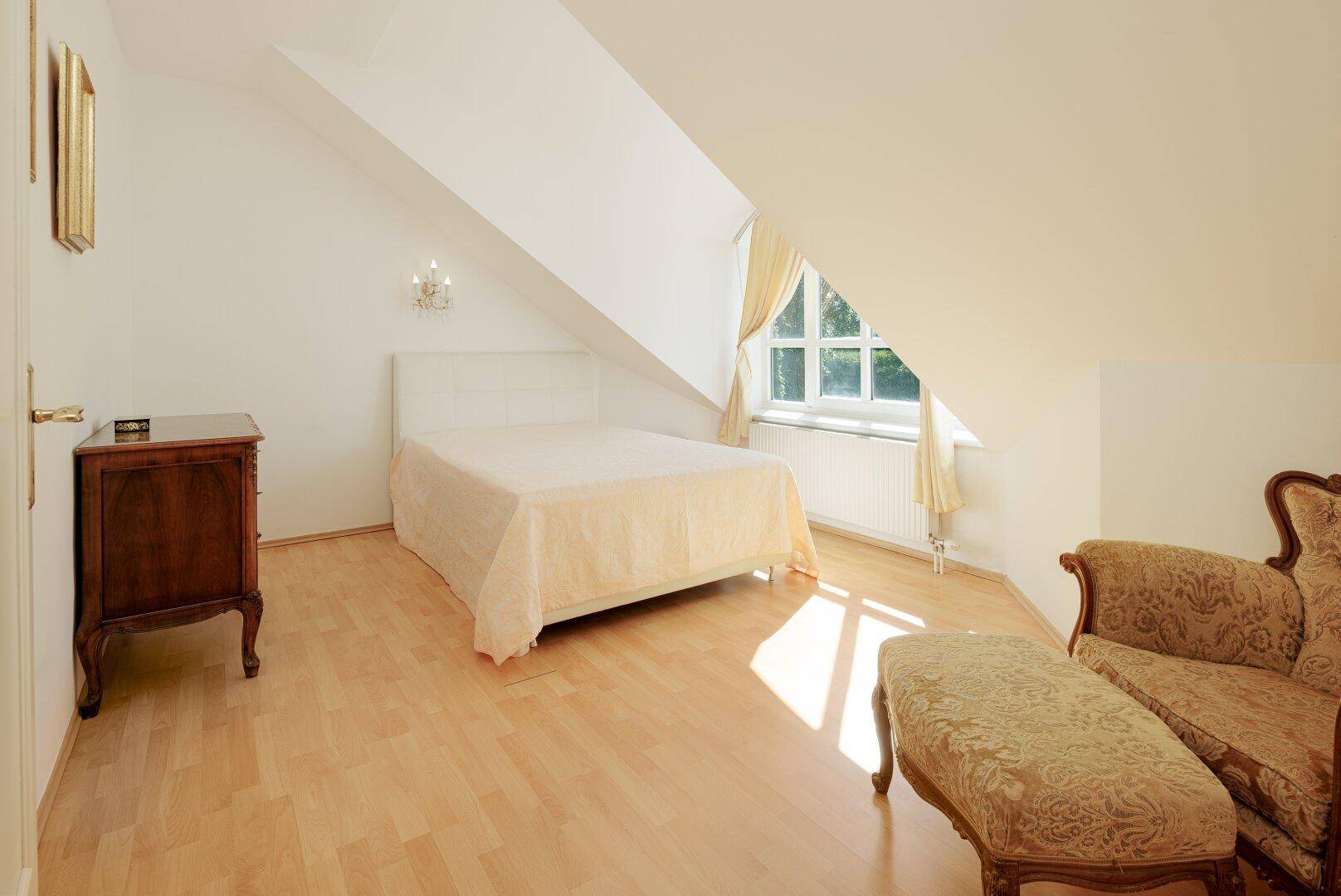 Helles Schlafzimmer im Dachgeschoss mit Holzboden, Fenster und klassischer Einrichtung.