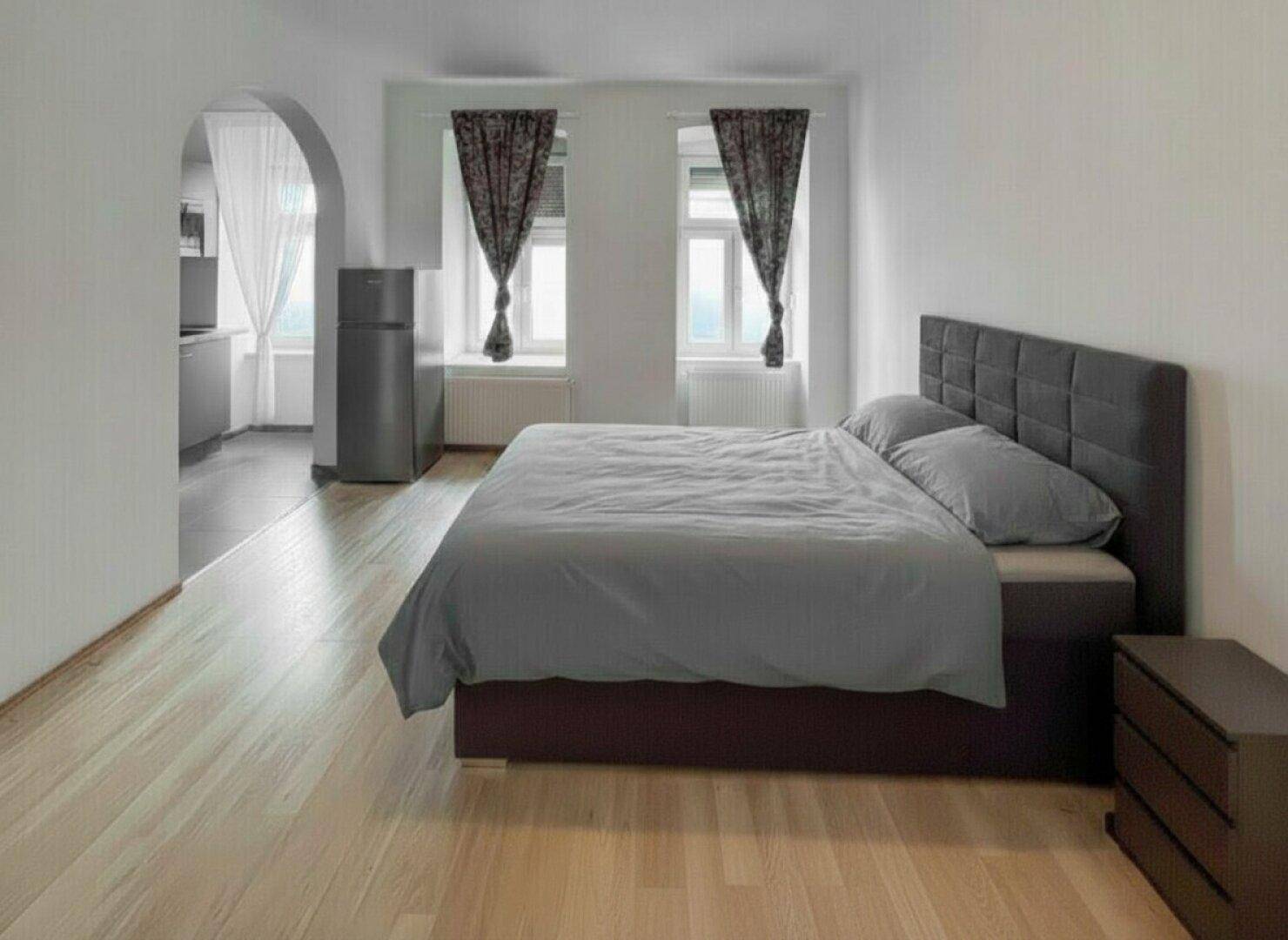 Helles Schlafzimmer mit Holzboden, großem Bett und Blick durch einen Bogen in einen weiteren Raum.