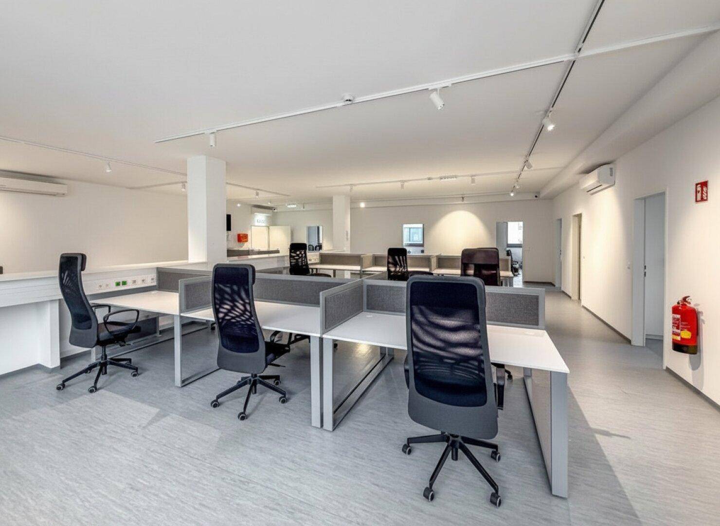 Offenes Büro mit ergonomischen Stühlen, modularen Schreibtischen und einem Feuerlöscher an der Wand.