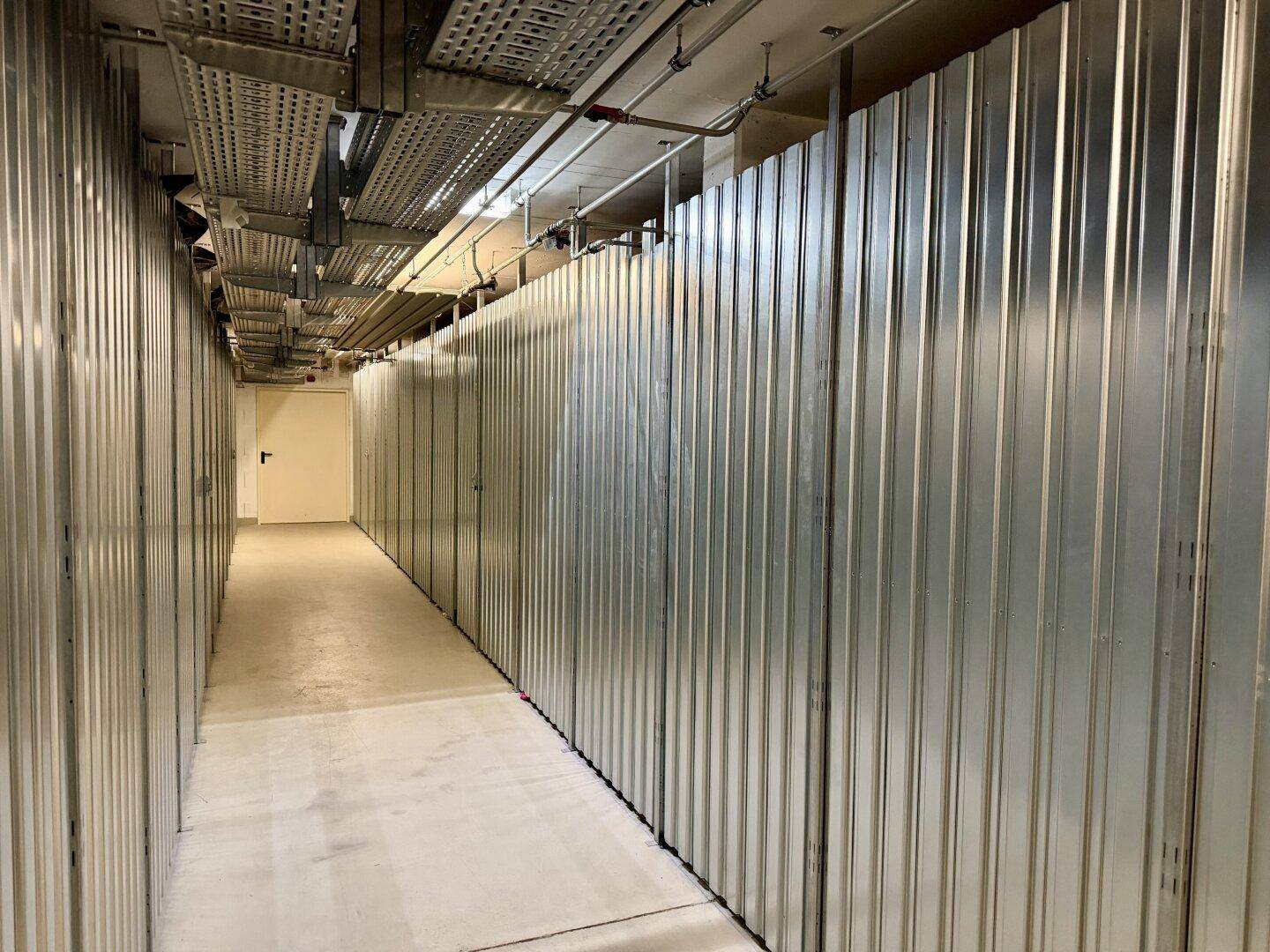 Langer Gang mit zahlreichen individuellen Lagereinheiten aus Metall, ideal für sichere Aufbewahrung.