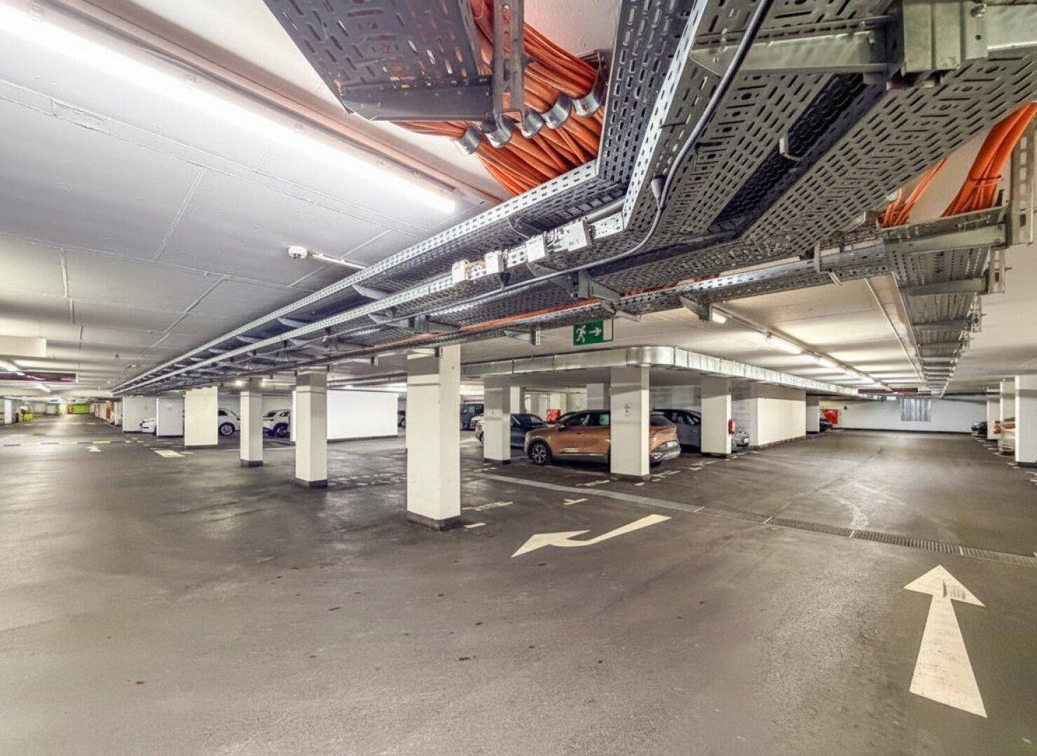 Geräumige Tiefgarage mit markierten Stellplätzen, guter Beleuchtung und sichtbaren Installationen an der Decke.