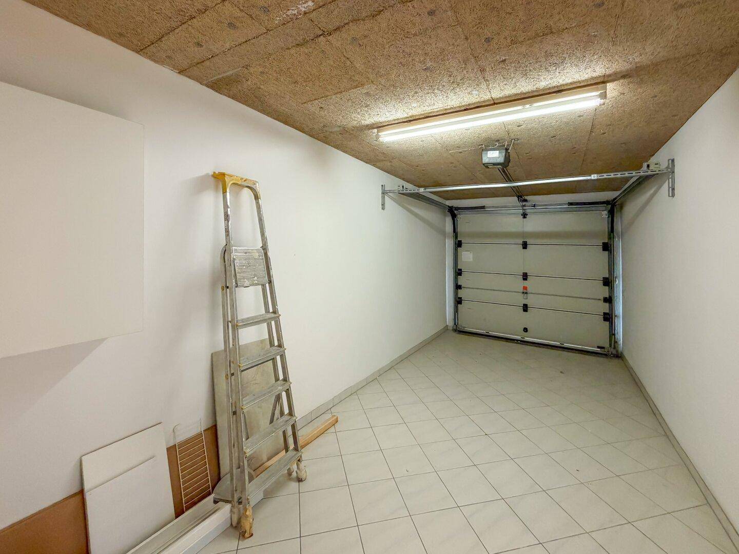 Geräumige Garage mit Fliesenboden, Leiter und automatischem Garagentor.