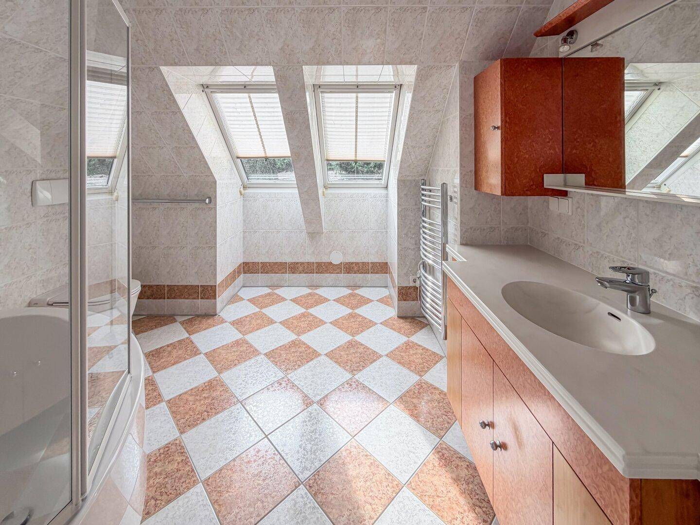 Helles Badezimmer im Dachgeschoss mit kariertem Fliesenboden, Dachfenstern und Dusche.