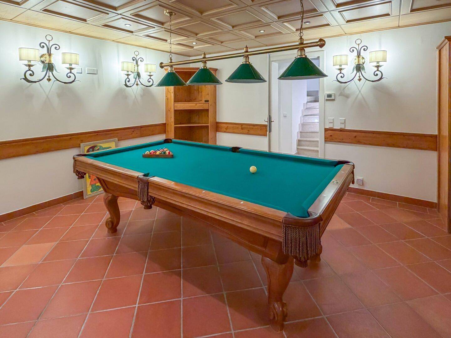 Spielzimmer im Untergeschoss mit Billardtisch, Fliesenboden und rustikaler Beleuchtung.