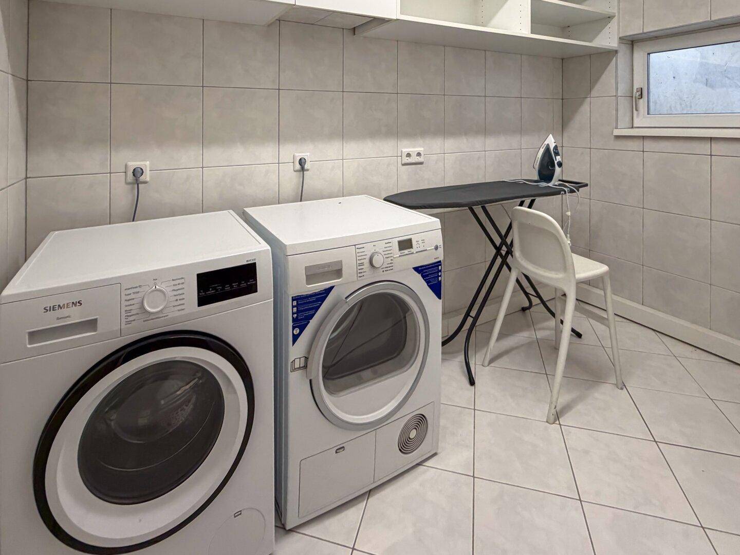 Praktischer Hauswirtschaftsraum mit Waschmaschine, Trockner und Bügelbrett.