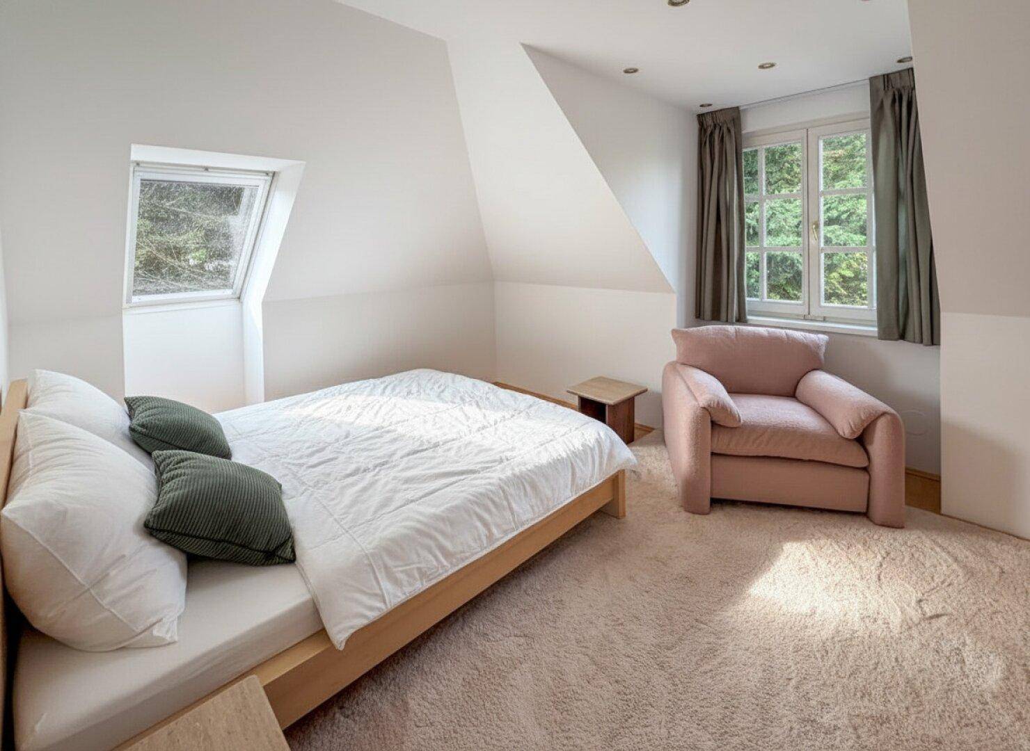 Schlafzimmer im Dachgeschoss mit Teppichboden, Dachfenster und gemütlichem Sessel.